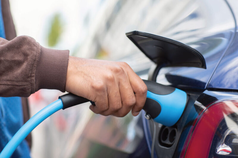 Hand mit Ladestecker an der Ladebuchse einen Elektroautos.