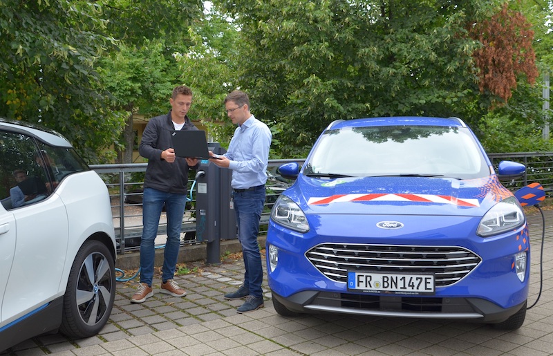 Zwei Männer mit Laptop stehen zwischen zwei Autos - Praxistest für Stromnetz und Ladesystem.