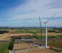 Eine Windkraftanlage während der Errichtung in einer flachen ländlichen Region mit Windpark am Horizont.