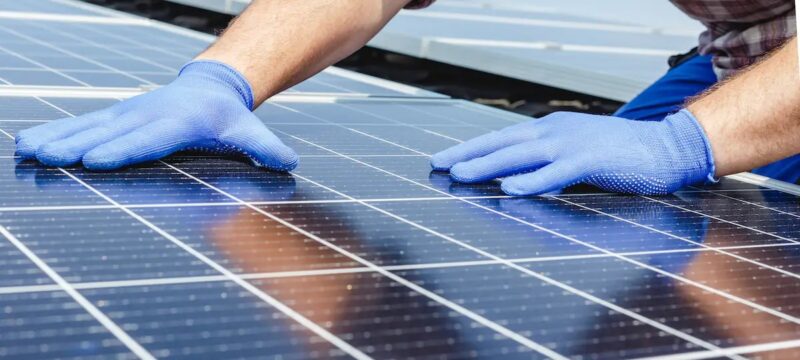 Im Bild zwei Hände mit blauen Handschuhen, die PV-Module behandeln.