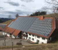 Ein landwirtschaftliches Gebäude in einer Hügellandschaft. In der Mitte auf dem Dach ist ein Luftkollektor zu sehen.