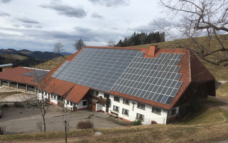 Ein landwirtschaftliches Gebäude in einer Hügellandschaft. In der Mitte auf dem Dach ist ein Luftkollektor zu sehen.