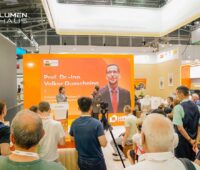 Zu sehen ist der Lumemhaus Stand auf der Intersolar mit einem Podium auf dem Prof. Dr. Volker Quaschning und Adrian Bühler zusammen diskutieren.