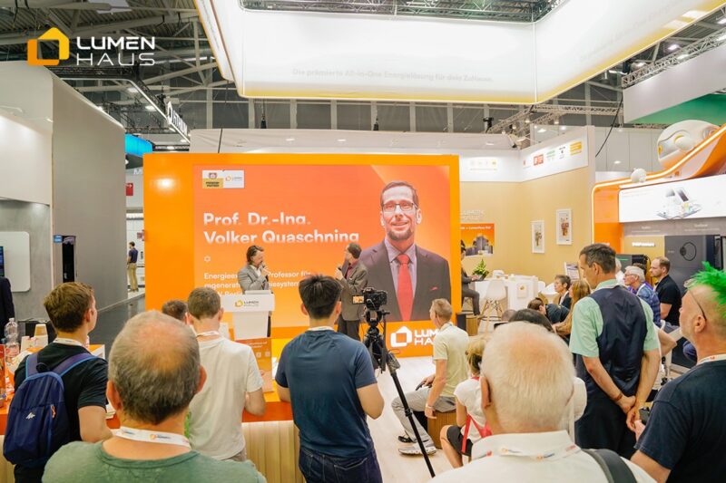 Zu sehen ist der Lumemhaus Stand auf der Intersolar mit einem Podium auf dem Prof. Dr. Volker Quaschning und Adrian Bühler zusammen diskutieren.