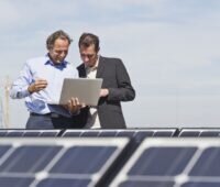 Zu sehen sind zwei Menschen inmitten einer großen PV-Aufdachanlage. Es handelt sich um eine der Photovoltaik-Anlagen der MVV.