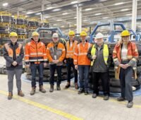 7 Personen in roten Schutzwesten in einer Halle mit Drahtrollen.