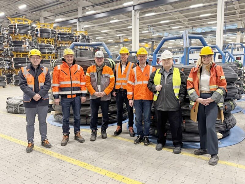 7 Personen in roten Schutzwesten in einer Halle mit Drahtrollen.