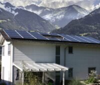 Ein Haus mit Solaranlage vor Bergkulisse, die Photovoltaik-Förderung in Österreich steht in der Kritik.
