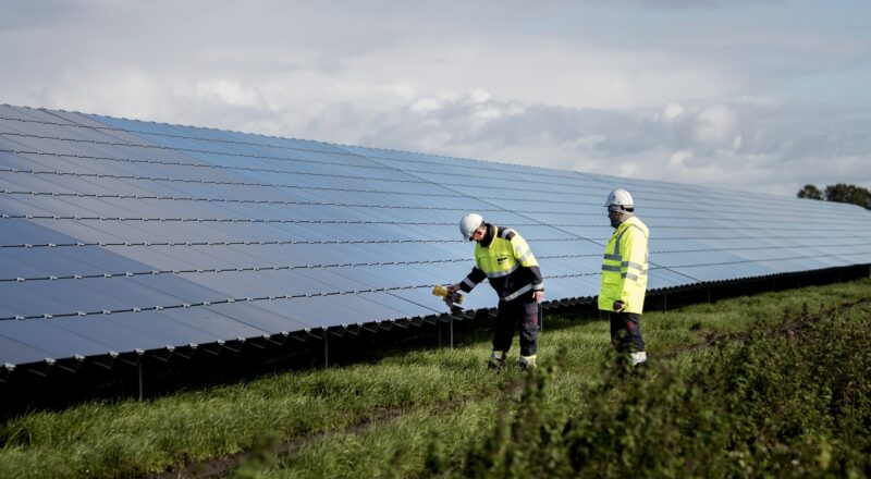 Zwei Menschen in gelber Arbeitskleidung inspizieren Solarmodule in einem Photovoltaik-Solarpark, Statkraft verkauft Solarstrom über einen Solar-PPA an die Wuppertaler Stadtwerke.