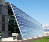 Zu sehen ist eine Solarfassade der Firmenzentrale von Meyer Burger, im HIntergrund die Alpen.