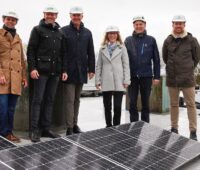 Menschen mit Bauhelmen auf einem Dach, vorne PV-Module - Einweihung von Mieterstrom-Anlage in Hamburg