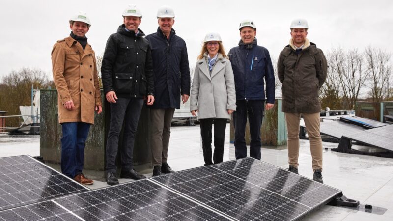 Menschen mit Bauhelmen auf einem Dach, vorne PV-Module - Einweihung von Mieterstrom-Anlage in Hamburg