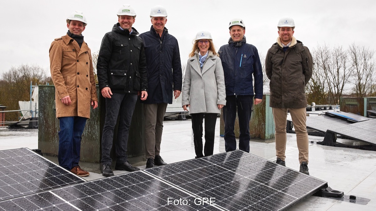 Menschen mit Bauhelmen auf einem Dach, vorne PV-Module - Einweihung von Mieterstrom-Anlage in Hamburg