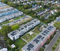 Luftaufnahme der Ossendorfer Gartenhöfe in Köln: Auf den Dächern mehrerer Wohngebäude sind Photovoltaikmodule zu sehen. Zwischen den Häusern liegen begrünte Innenhöfe.