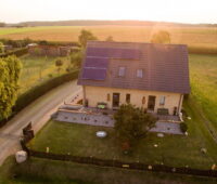 Ein freistehendes Einfamilienhaus auf dem Lande beim Sonnenuntergang, von oben fotografiert mit Blick auf Spitzdach mit PV-Anlage.