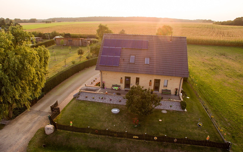 Ein freistehendes Einfamilienhaus auf dem Lande beim Sonnenuntergang, von oben fotografiert mit Blick auf Spitzdach mit PV-Anlage.