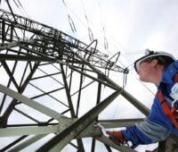 Zu sehen ist ein Mitnetz Mitarbeiter an einem Hochspannungsmast. Für die automatisierte Netzanschluss-Prüfung ist nun kein Mitarbeiter mehr nötig.