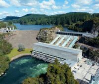 Das Foto zeigt ein Wasserkraftwerk in einer bewaldeten Hügellandschaft, dass einen Fluß in ein Oben und ein Unten teilt.