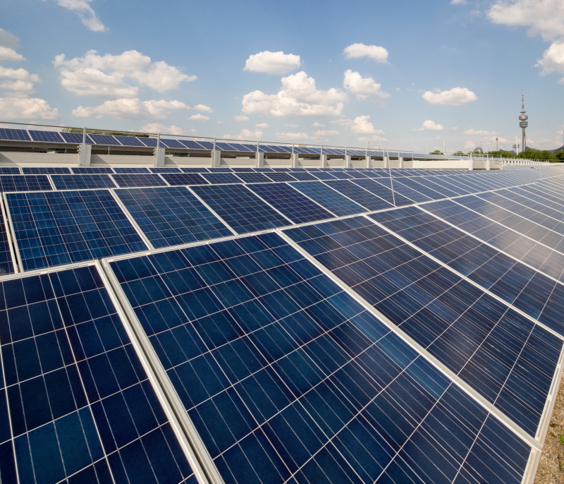 Eine Solaranlage auf einem Flachdach. Im HIntergrund der Münchener Olympiaturm.