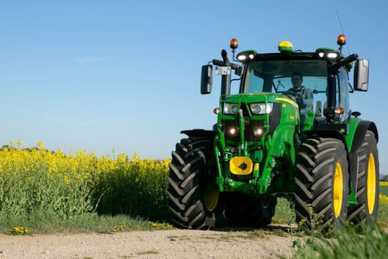 Ein Traktor fährt an einem Rapsfeld entlang.