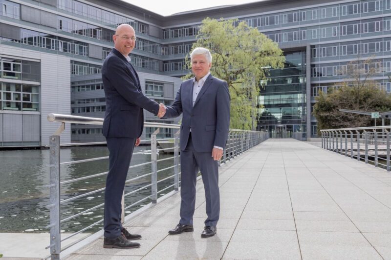 Zwei Männer in Anzügen reichen sich auf einem Firmendach die Hand.