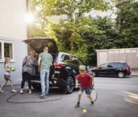 Zu sehen ist eine Familie mit E-Auto, die Netzintegration von Elektromobilität soll zugleich netzdienlich sein.