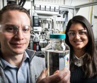 Die Forscher Derek Vardon und Nabila Huq zeigen eine Behälter mit dem Biokraftstoff.