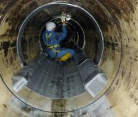 Arbeiter hockt in einem Kanalrohr und montiert einen Wärmetauscher, Initiative Abwasserwärme NRW will Abwassernutzung voranbringen.