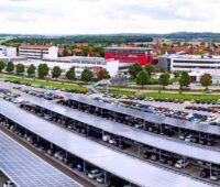 Zu sehen ist ein mit PV-Modulen überdachter Firmenparkplatz mit hunderten von Parkplätzen. Die Photovoltaik-Pflicht für neue Parkplätze in NRW soll ab 35 Stellplätzen greifen.