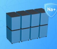Computeranimation eines modular aufgebauten Heimspeichersystems mit acht blau-grauen Batteriemodulen vor blauem Hintergrund. Rechts daneben ist ein Schutzschild mit der Aufschrift „Na+“ als Hinweis auf die Natrium-Ionen-Technologie dargestellt.