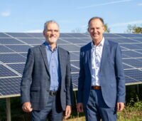 Zwei Männer in Anzügen vor PV-Anlage im Freien