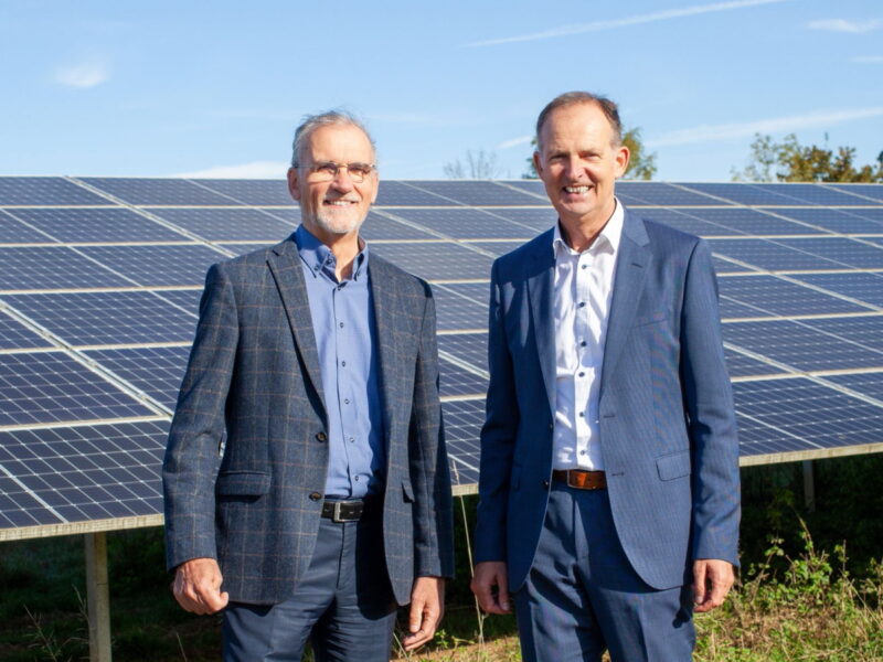 Zwei Männer in Anzügen vor PV-Anlage im Freien