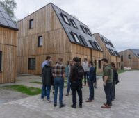 Mehere Personen vpr Holzhäusern mit dachintegrierter PV.