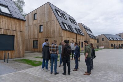 Mehere Personen vpr Holzhäusern mit dachintegrierter PV.