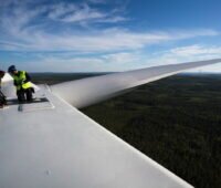 Zwei Arbeiter auf der Nabe einer Windkraftanlage in luftiger Höhe.