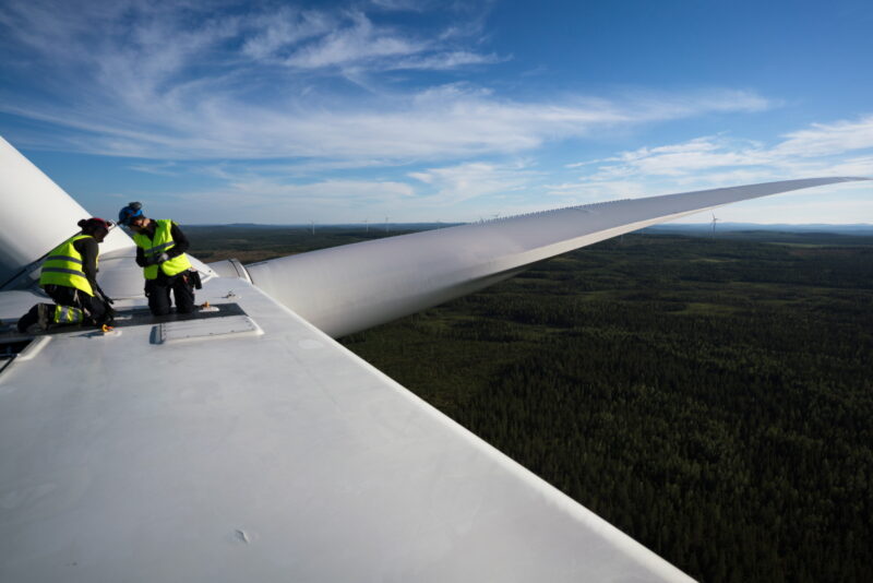 Zwei Arbeiter auf der Nabe einer Windkraftanlage in luftiger Höhe.