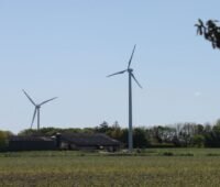 Eine Kleinwindanlage auf einem Hof in Schleswig-Holstein. Im Hintergrund eine Großwindkraftanlage.