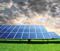 Ein Freiflächensolarpark unter bewegtem Himmel und auf grüner Wiese.