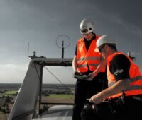 Zwei Männer in roten Sicherheitswesten auf der Gondel einer Windenergieanlage in großer Höhe.