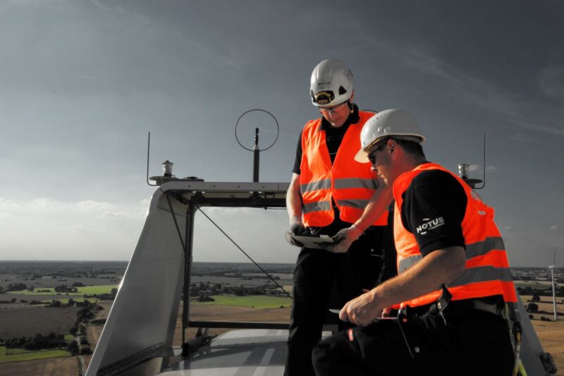 Zwei Männer in roten Sicherheitswesten auf der Gondel einer Windenergieanlage in großer Höhe.