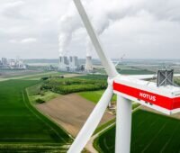 Luftaufnahme zeigt eine Windenergieanlage vor Braunkohlekraftwerk im Hintergrund.