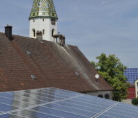 Ein alter Kirchturm hinter PV-Dach-Flächen.