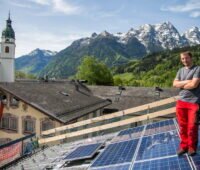 Eine PV-Dachanlage mit Monteur in einem Dorf vor dem Hintergrund schneebedeckter Alpen.