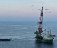 Ein Offshore-Installationsschiff mit großem Kran arbeitet auf ruhiger See an der Errichtung des Windparks Nordlicht I. Daneben liegt ein Versorgungsschiff; im Hintergrund ist die offene Nordsee zu sehen.
