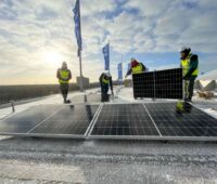 Auf dem Dach des Olympiastadions in Berlin montieren Arbeiter bei tief stehender Sonne Solarmodule.