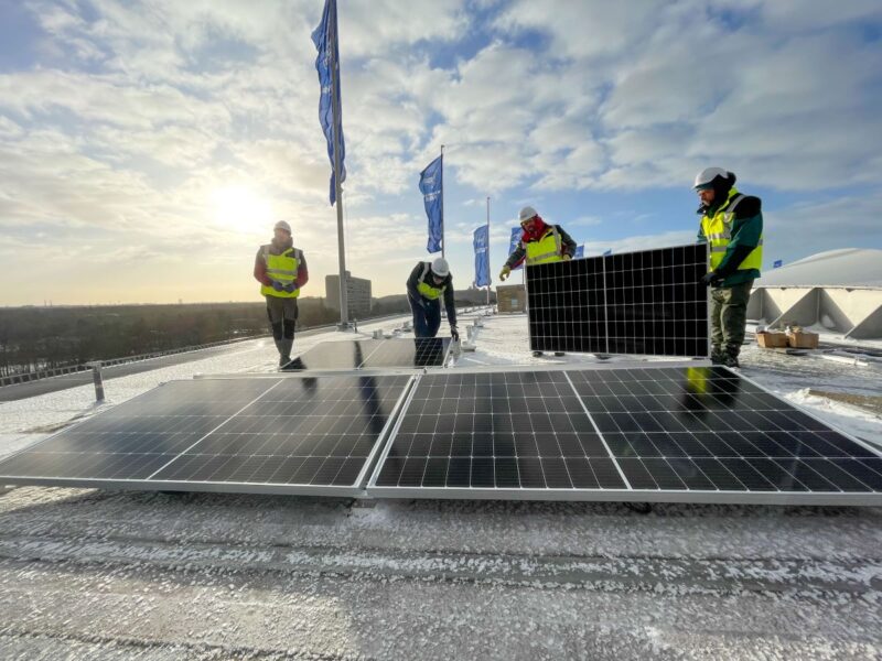 Auf dem Dach des Olympiastadions in Berlin montieren Arbeiter bei tief stehender Sonne Solarmodule.