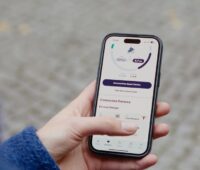 Im Bild eine Hahd mit Handy mit der Ostrom-App, über die man ein Virtuelles Kraftwerk für E-Autos nutzen kann.