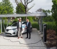 Zwei Männer mit Elektroauto präsentieren eine Broschüre.