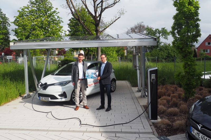 Zwei Männer mit Elektroauto präsentieren eine Broschüre.