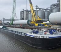 Ein Kran hebt die Stahlturmsektionen der Enercon-Windturbinen vom Schubleichter. Der Transport von Windturbinen-Komponenten auf Wasserwegen bietet Vorteile.